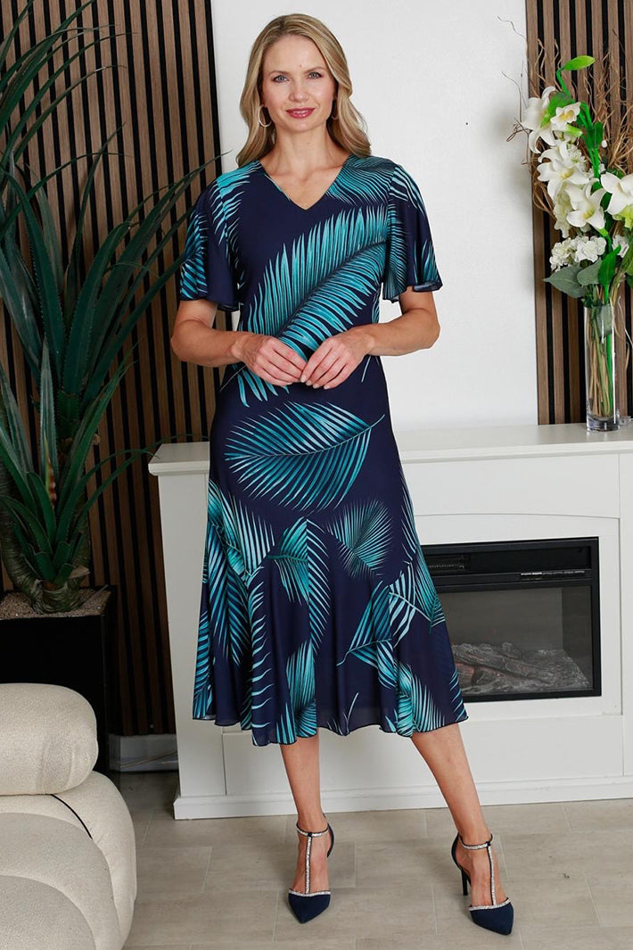 Woman wearing a blue and green leaf-patterned dress in a living room setting.