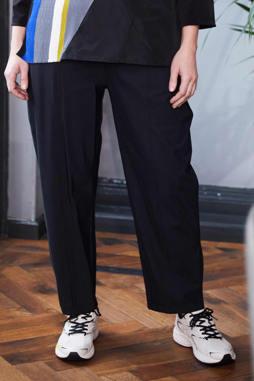 Person wearing black pants and white sneakers on a wooden floor.